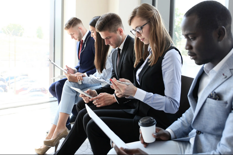 A group of five professionally dressed people sitting in a row, reviewing documents.