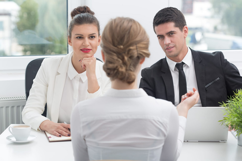 Three people are engaged in a discussion, with two of them facing the third person across a desk.