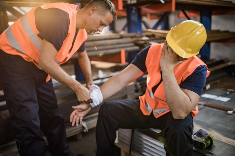 A construction worker tends to his injured colleague's arm as the injured worker holds his head in pain.